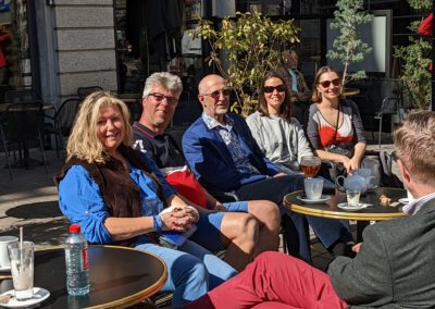 A group of people sat outside at a café in France with small round tables enjoying some drinks.