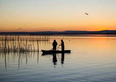 Two people silhouetted fishing on a calm lake just after sunset