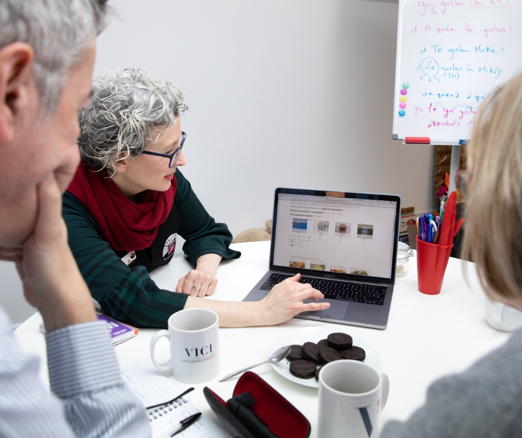 A woman with curly hair teaching two adult students at the VICI academy with an open laptop at a table