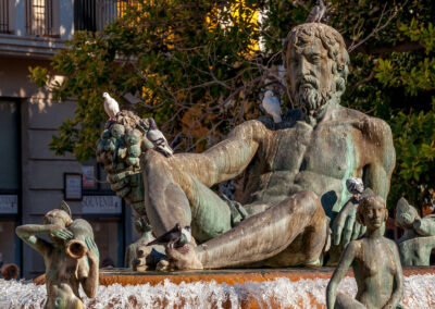 A statue of a man lying down with a beard on top of a fountain - Plaza de la Virgen