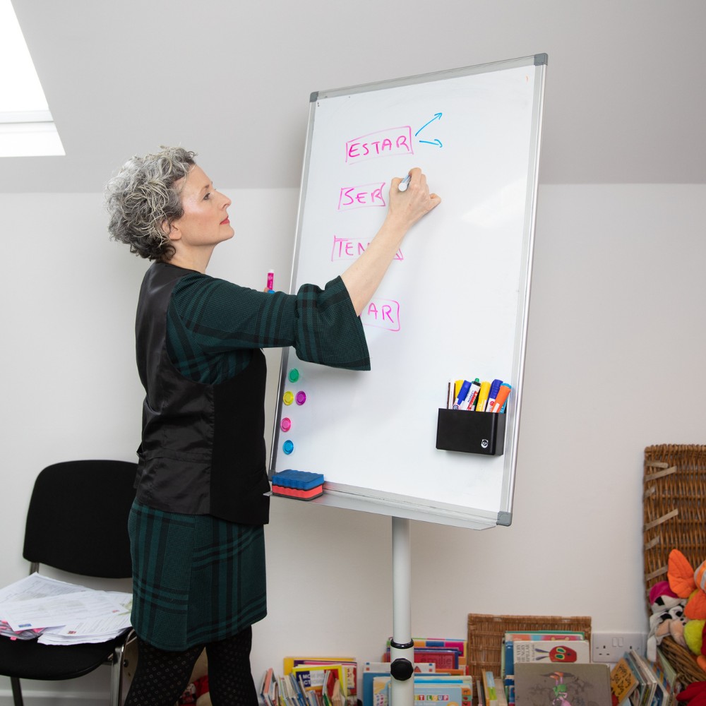A teacher coaching Spanish and writing verbs on a whiteboard