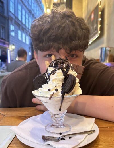 A young boy hiding behind a tall ice cream dessert