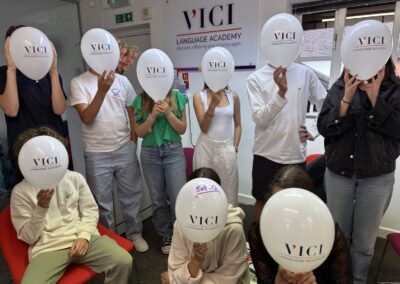 A group of students holding 'VICI' balloons in front of their faces