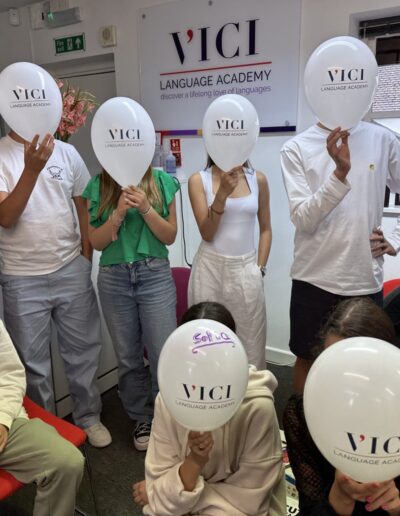 A group of students holding 'VICI' balloons in front of their faces