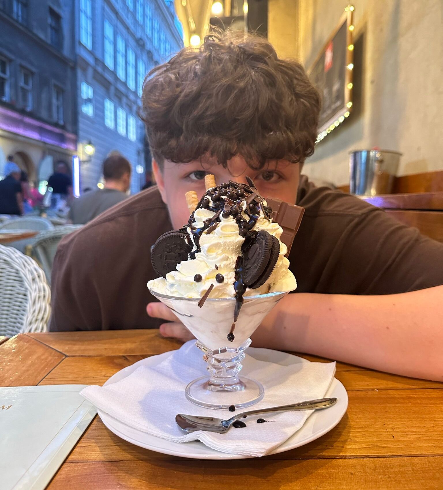A teenager hiding behind a large icecream dessert on a European street