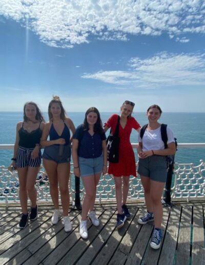 A group of teenage girls stood on a boardwalk in front of a blue ocean on a summers day