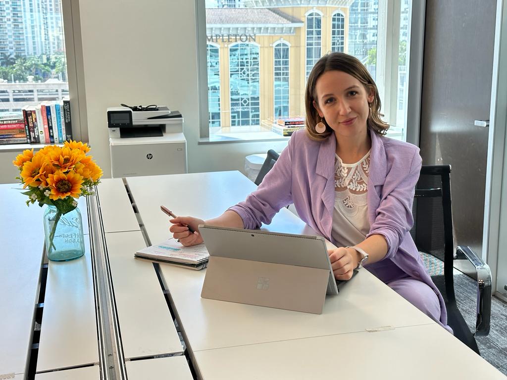A woman in a purple jacket sat at a desk with flowers