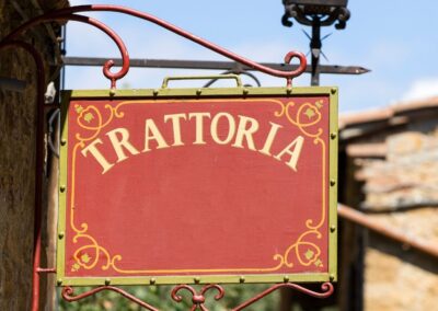 A red trattoria sign with gold writing hung on a building